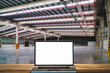 Open blank screen laptop computer on wooden table at empty factory background.