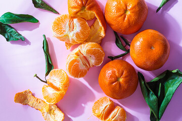 Wall Mural - Peeled and unpeeled fresh tangerines on pink background.