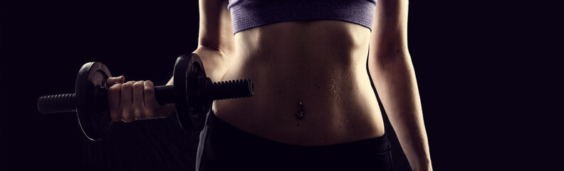 Slim athletic woman Holding dumbbell in the hand on black