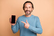 © deagreez - Photo portrait of middle-aged man pointing finger cellphone display copyspace smiling isolated on pastel beige color background