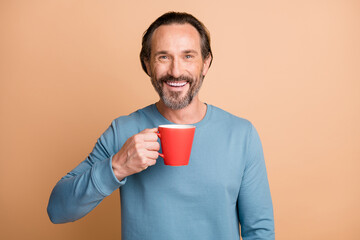 Poster - Photo of positive mature man hold cup toothy smile wear blue pullover isolated beige color background