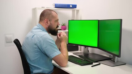 Man typing on the keyboard on two monitors with the green screen. remote work at home