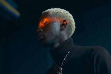 portrait of a dark-skinned handsome guy with white hair dressed in a brown sweater over which hangs 