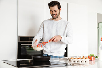 Happy handsome young man smiling while cooking scrambled eggs