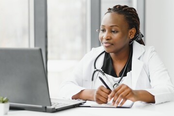 Wall Mural - medicine, online service and healthcare concept - happy smiling african american female doctor or nurse with headset and laptop having conference or video call at hospital