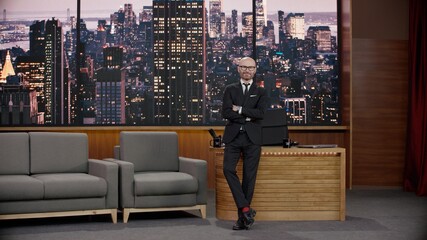 Wall Mural - Late-night talk show host is leaning against his table in studio, looking into camera. TV broadcast style show