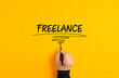 Male hand writing freelance on yellow background. Freelance job or working as a freelancer concept..