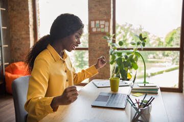 Canvas Print - Photo portrait of african american excited girl celebrating working on laptop in modern office indoors