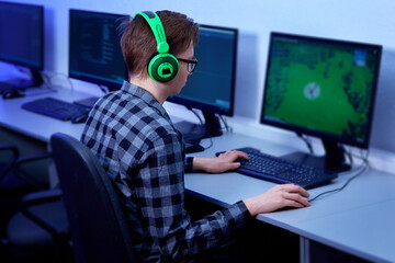 A professional gamer plays the game online on his personal computer. Bright green headphones.