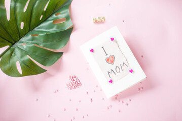 a card from a child with a congratulation on mom's day on a pink background with tropical green leaf.