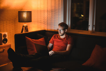 Portrait of attractive nerdy man is working late night on the computer in living room in home office