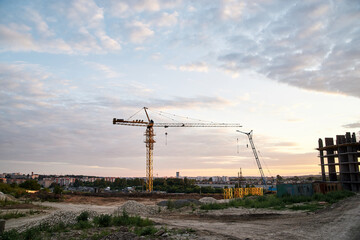 Beautiful city view at sunset. Industrial town landscape in the evening. Construction site with crane in front of blue pink cloudy sky.