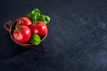 Fresh grape tomatoes with spinach Leaves on black stone background. Vegan veggies diet food. Herb, red tomatoes, cooking concept.