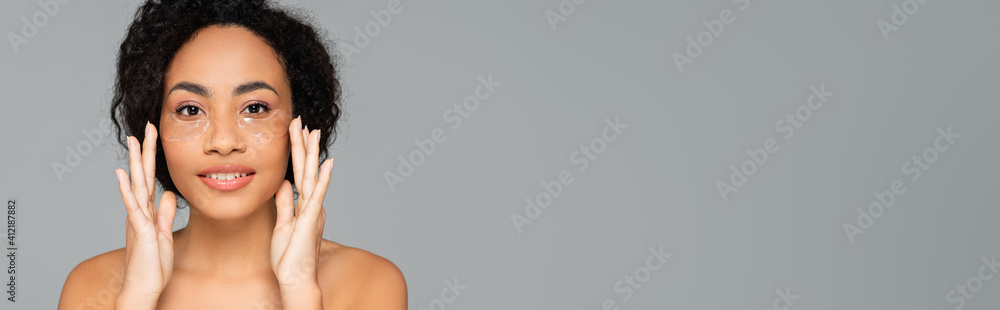 African american woman with naked shoulders applying eye patches isolated on grey, banner - obrazy, fototapety, plakaty 