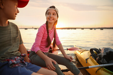 Poster - Happy children sitting on kayak near river at sunset. Summer camp