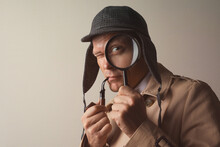Male Detective With Smoking Pipe Looking Through Magnifying Glass On Beige Background. Space For Text