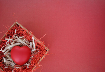 Red heart in a box with cut paper shavings on a red background  