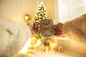 Poster - Woman with cup of drink and blurred Christmas tree on background, closeup