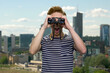 © DenisProduction.com - Shocked young teen boy looks through binoculars. Urban cityscape on the background.