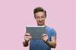 © DenisProduction.com - Smiling american guy looking at the tablet. Caucasian schoolboy isolated on pink background.
