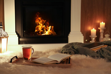 Wall Mural - Cup of tea and book on fuzzy rug near fireplace at home. Cozy atmosphere