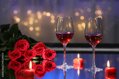 Glasses of wine, candles and roses on table against blurred lights. Romantic dinner for Valentine\'s day