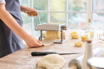 Woman making pasta with machine on table in kitchen