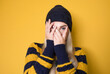 © Alen-D - Young woman listen bad news. Shocked girl covering mouth with hands for mistake and stare to you with popped eyes, model wearing woolen cap and sweater, isolated on yellow background. Scared female