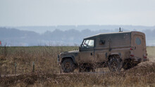 British Army Land Rover Defender 4x4 Speeds Along A Dusty Dirt Track With Light Snow Falling