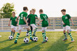 © matimix - Group of children playing soccer on training session. Kids in football club wearing blue jersey shirts and soccer kits. Happy boys practicing football with coach on a sunny day