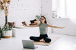 © nikkimeel - Beautiful brunette fitness woman make stretching exercises in front laptop, doing yoga indoors at home. Staying fit and healthy