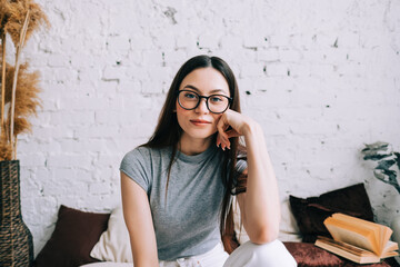authentic lifestyle portrait of attractive young caucasian woman in eyeglasses sitting on a sofa at 