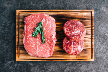 Wall Mural - Raw beef steak and minced round steak for burgers on wooden board, top view .