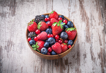 Wall Mural - Berries fresh vibrant front view arrangement in wooden jar mix of blackberries, blueberries, strawberries, raspberries and red currant on old white wooden table studio shot