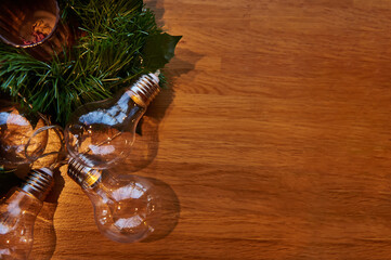 Flat lay composition with ornament of transparent lamps on a pine branch lying on a wooden board with copy space