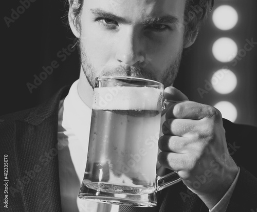 Man or businessman hold beer glass. Handsome bearded hipster holds glass of beer. Beer pub. Stylish guy at cafe pub. Cheerful young man drinks beer at the bar counter.