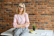 © Vadim Pastuh - Portrait of an elegant stylish mature middle-aged blonde businesswoman, ceo in glasses standing in the modern office and posing against the brick wall with the arms folded and looking at the camera