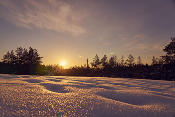 Snow in the foreground on a frosty winter evening at sunset as a backdrop and blurred forest on the background.