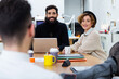 © Guille Faingold/Stocksy - Businesspeople smiling at their colleague sitting against them at desk.