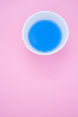 Wall Mural - Vertical shot of blue liquid watercolor paint on a bowl isolated on pink background