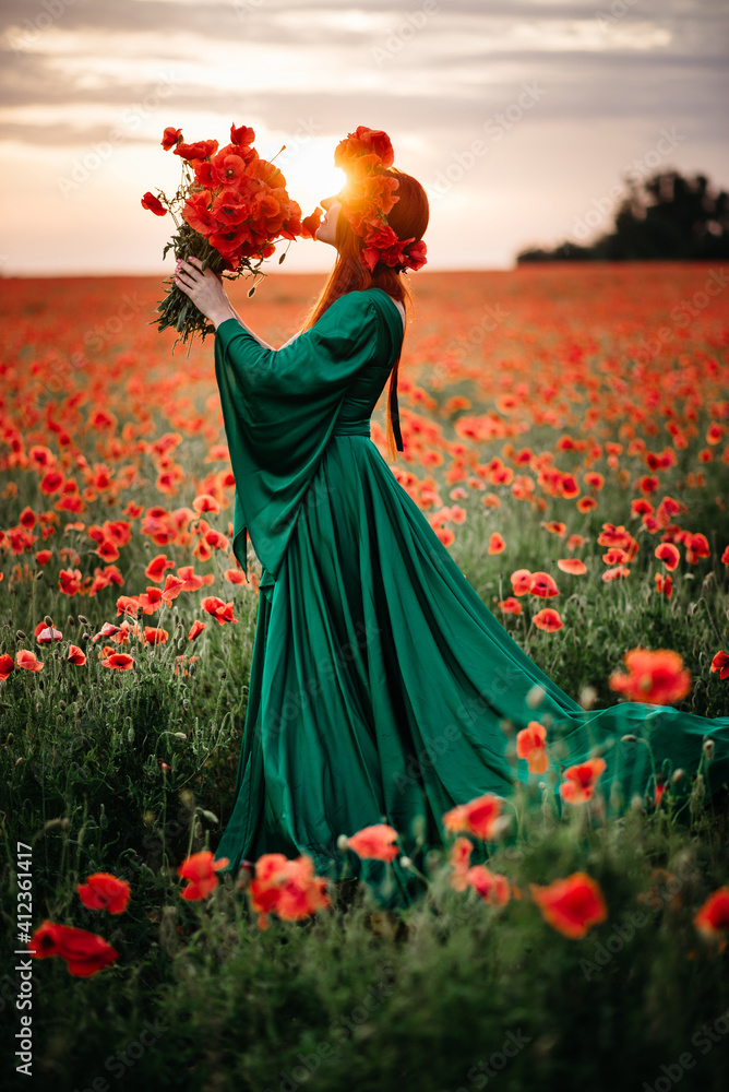 A young red-haired woman in a wreath stands in a blooming poppy field in the sun. Full-length portrait. - obrazy, fototapety, plakaty 