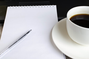 A notebook with a white blank sheet next to a white cup of coffee. A break at work