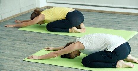 Two Caucasian good shape female Yoga players doing body stretches and practice together. Idea for self healthcare and balance of body and mind