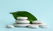 © FotoHelin - Minimalist beauty products background concept. Gray color flat sea stones stacked like an pedestal with palm leaf on against blue background.
