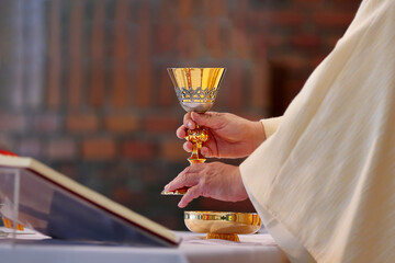 Chalice in the hands of the priest on the altar during the celebration of the mass