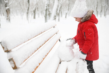 Poster - Cute little girl rolling snowball on bench in winter, space for text