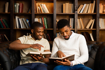 two young african men are sitting on the sofa with books 