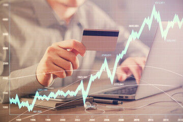 Double exposure of man hands holding a credit card and Forex graph drawing. Stock trading and digital fintech in Internet E-commerce concept.