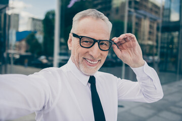 Photo of good mood mature worker man wear formal shirt arm eyeglasses tacking selfie outdoors city street