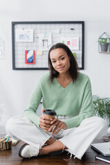 Canvas Print - young african american architect sitting on desk with coffee to go and looking at camera